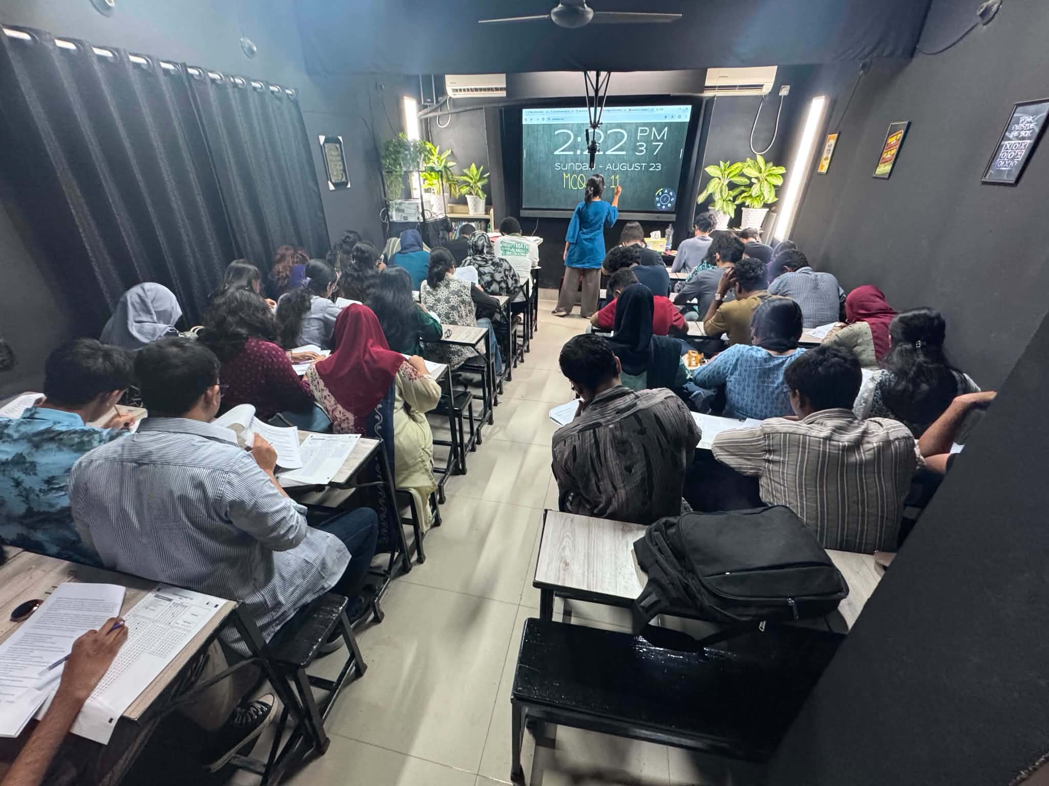 Students taking an offline mock test in a full classroom while an instructor stands at the front